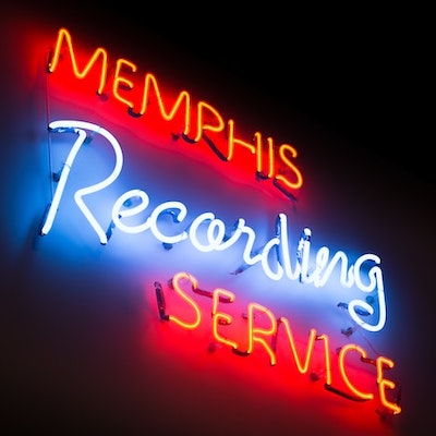 A neon sign hanging on a dark wall that says memphis recording service